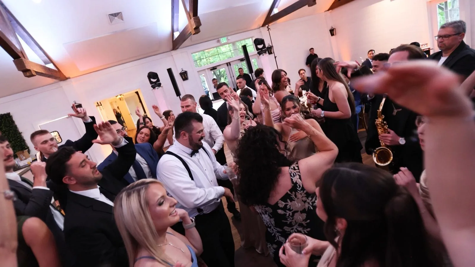 A packed dance floor in the barn at The Inn at Millrace Pond — guests dancing under the exposed beams while a live saxophonist plays alongside the DJ