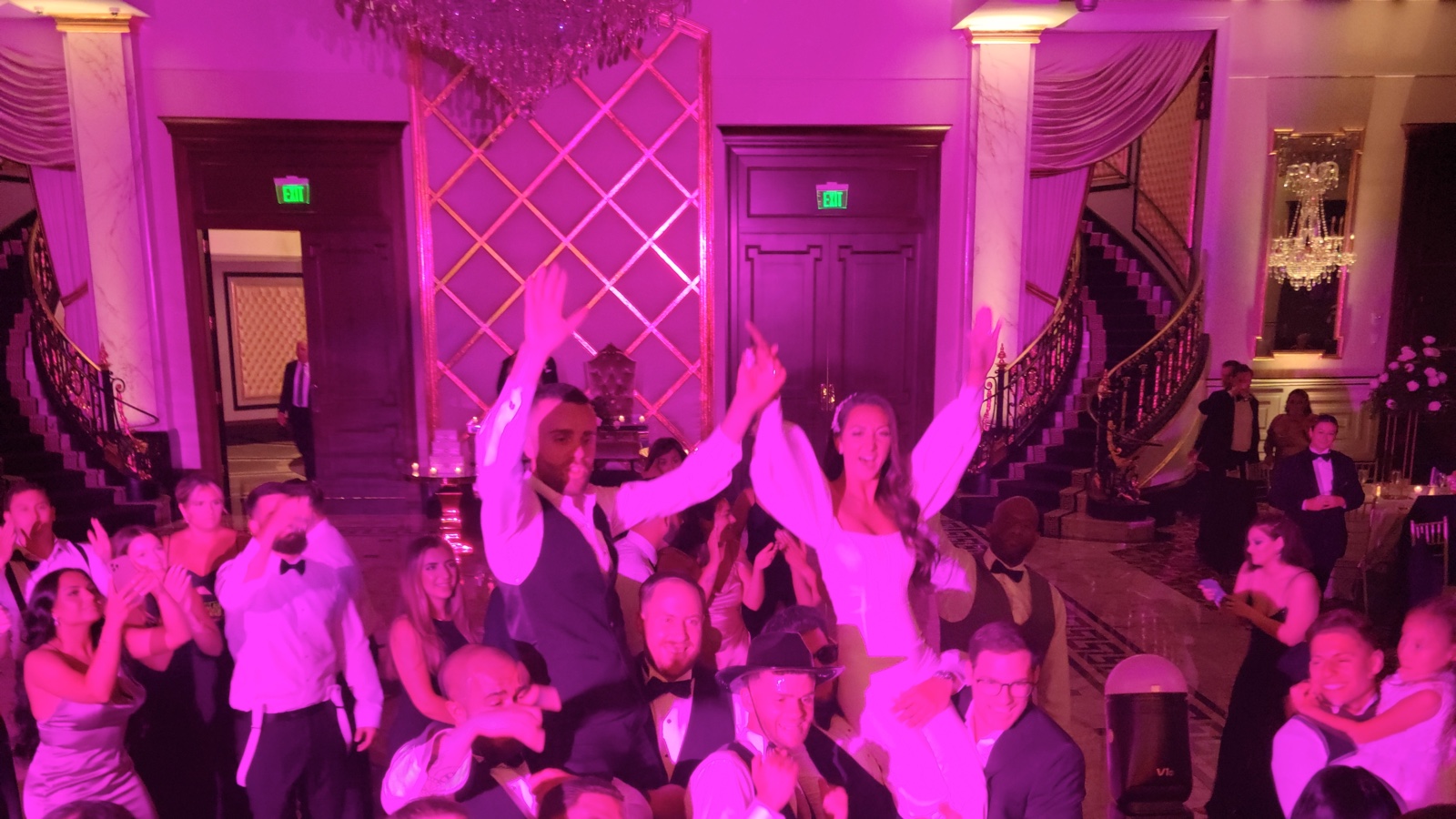 A packed dance floor under magenta lighting in the Grand Ballroom at Shadowbrook at Shrewsbury, with the staircase and chandelier behind