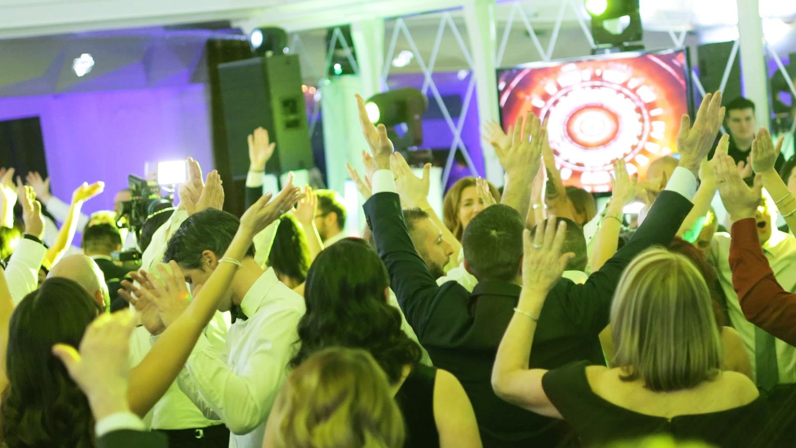 A packed dance floor with hands in the air at The Westmount Country Club, lit in purple with the lighting truss and LED screen behind